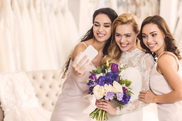 Happy women in wedding dresses taking selfie in wedding atelier